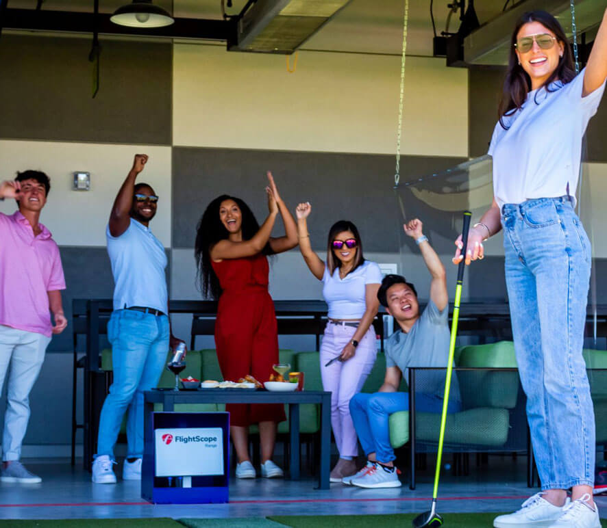 Indoor golf game in progress, players taking swings in a room with golf clubs and balls on the floor.