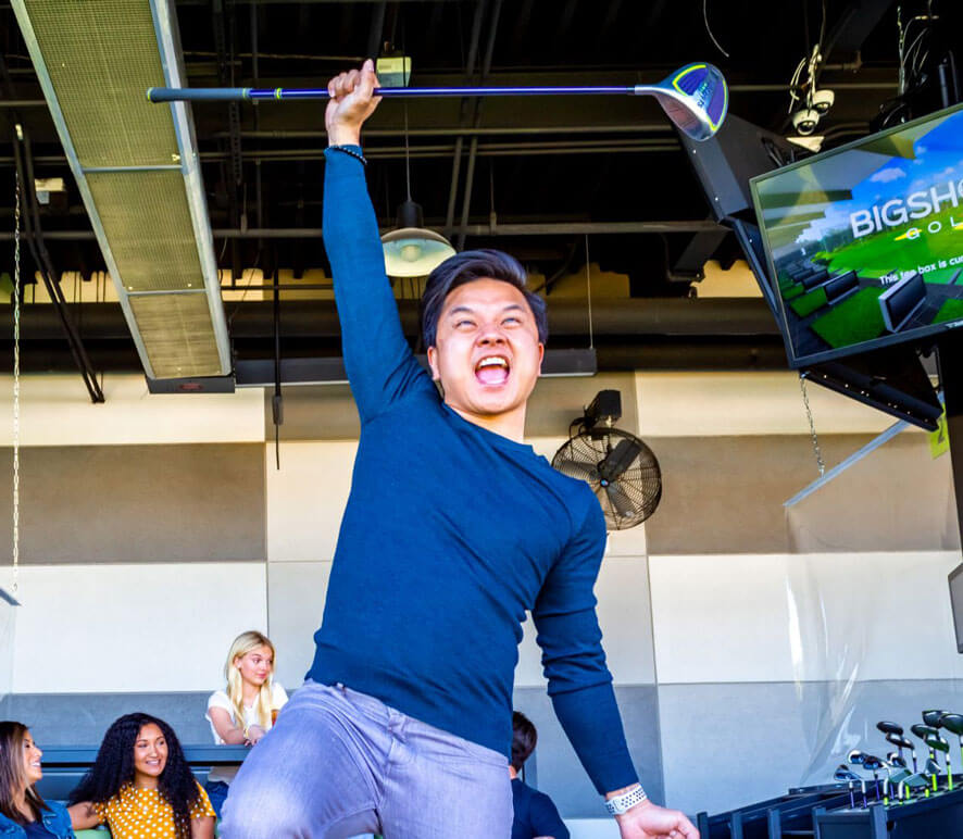 Man wearing a blue shirt and jeans, smiling while playing golf outdoors.