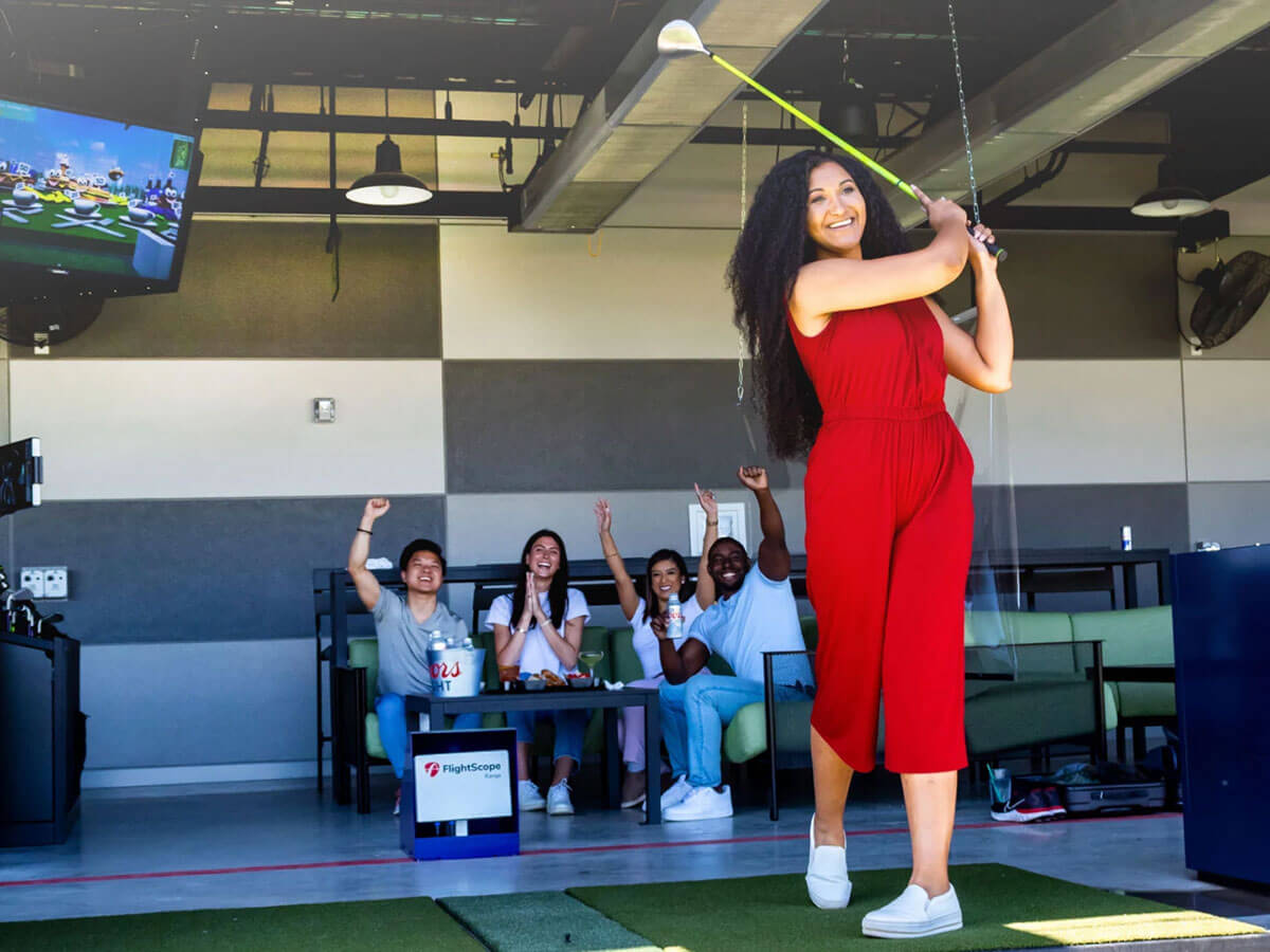 A woman in red swinging a golf club.